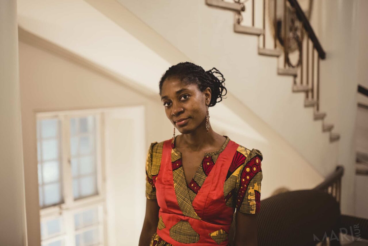 Photo de Rosine Mbakam, une femme noire mince, dans une robe colorée avec les cheveux attachés.