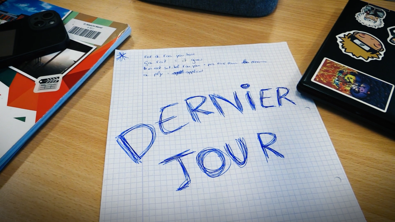 Feuille sur un bureau d'école où il est écrit "Dernier jour"